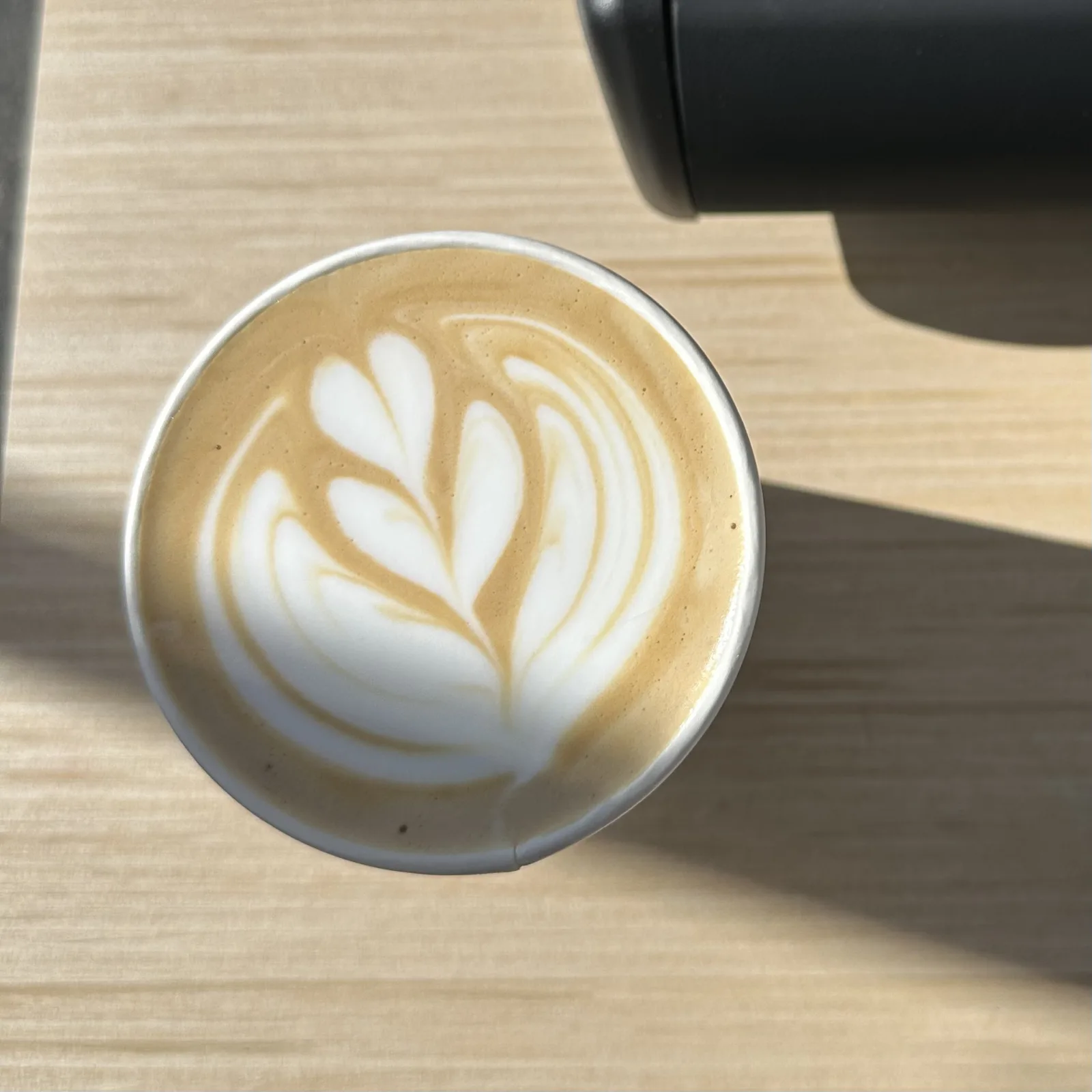 A hot latte finished with rosetta art, poured to order at an Esencia Coffee catering setup.