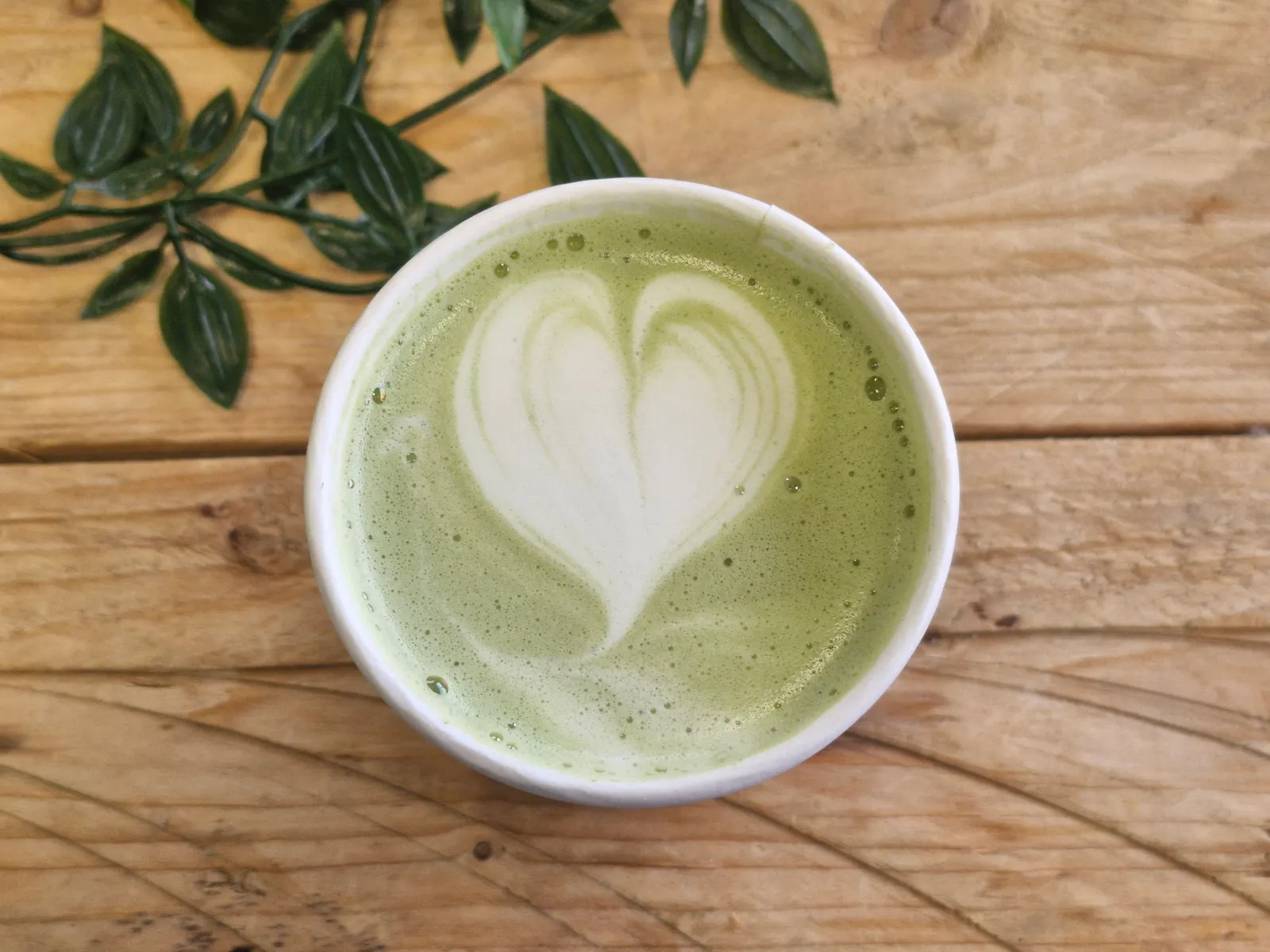 A hot matcha latte with heart latte art from the Esencia Coffee mobile coffee cart, on the Esencia Cl&aacute;sico Menu.